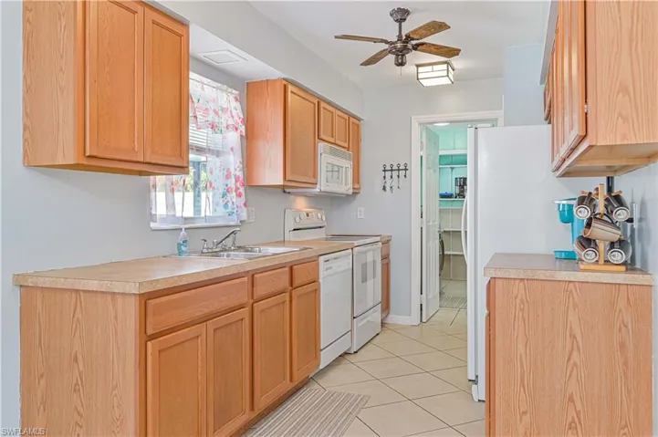 Kitchen featuring light tile patterned floors, white appliances, sink, and ceiling fan