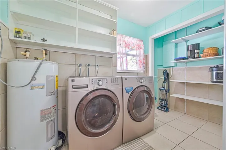 Laundry room with water heater, washer and dryer, tile walls, and light tile patterned floors