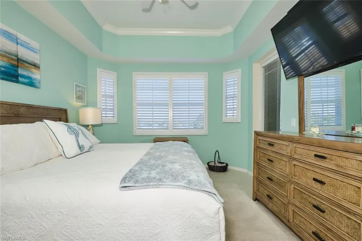 Bedroom with ceiling fan, ornamental molding, light colored carpet, and a tray ceiling