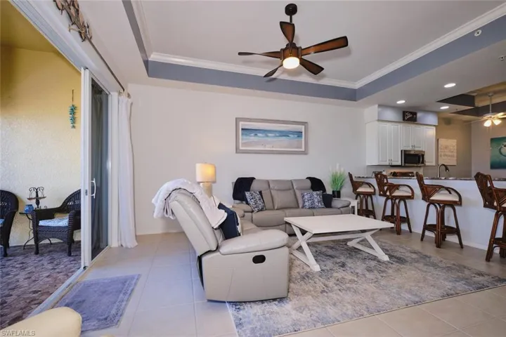 Living room featuring ceiling fan, a tray ceiling, ornamental molding, and light tile patterned flooring