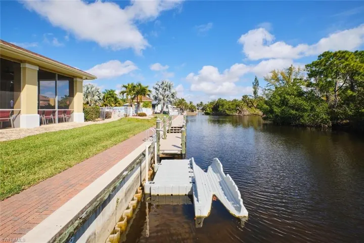 Dock area with a water view, a sunroom, and a lawn
