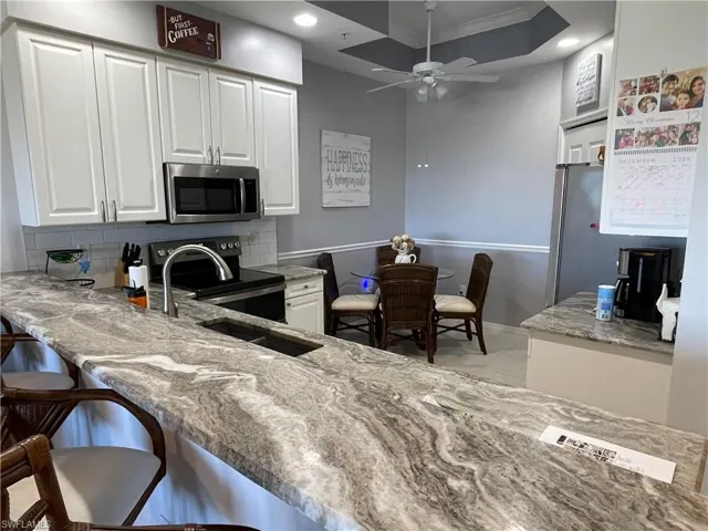 Kitchen with white cabinetry, stainless steel appliances, light stone countertops, recessed lighting, and backsplash