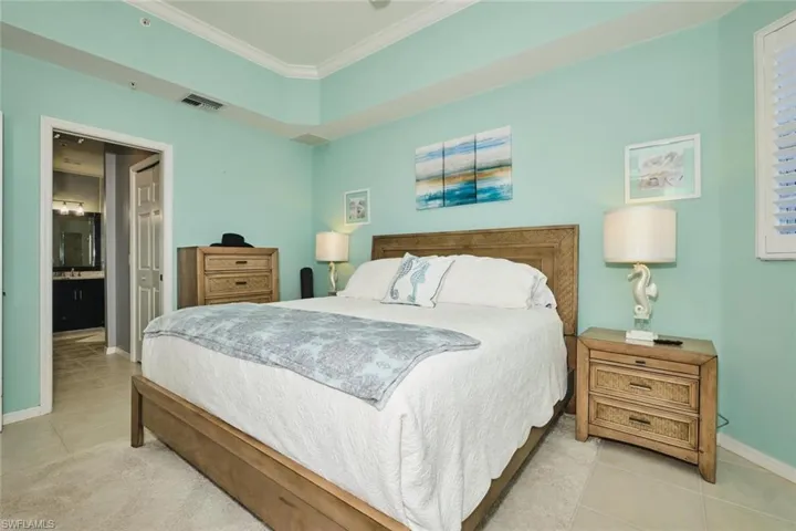 Bedroom with ornamental molding, ensuite bath, and light tile patterned flooring