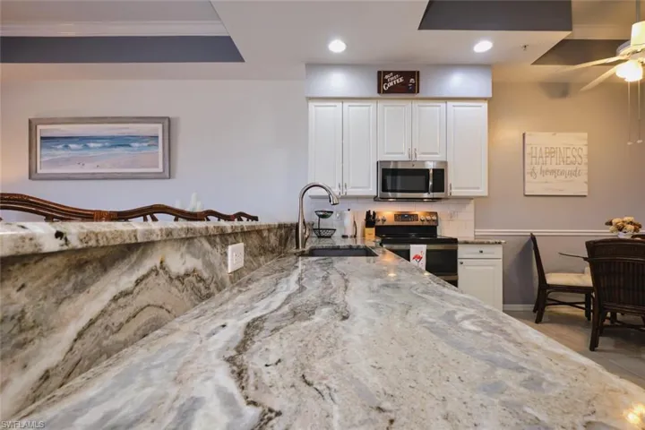 Kitchen featuring light stone countertops, white cabinets, backsplash, stainless steel appliances, and a ceiling fan