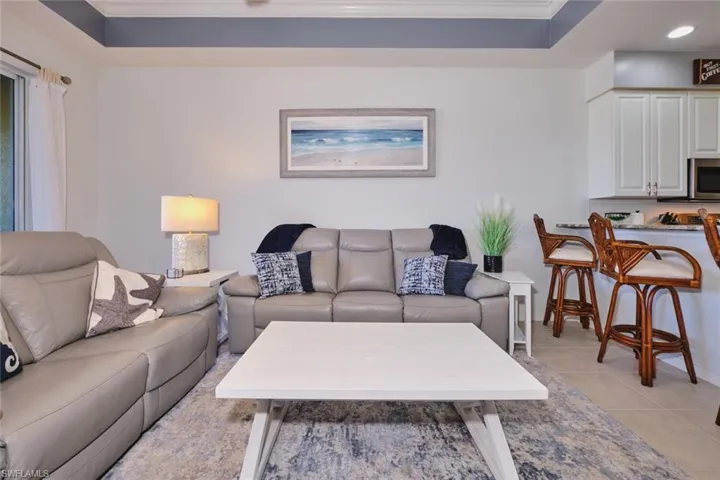 Living area with ornamental molding, light tile patterned floors, a tray ceiling, and recessed lighting