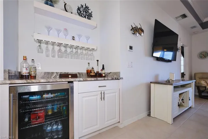 Indoor dry bar featuring beverage cooler, white cabinets, dark stone counters, and open shelves