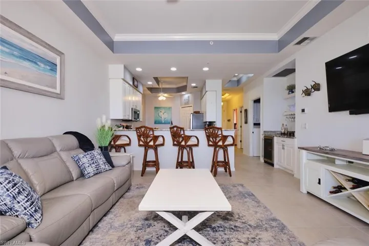 Living room with a raised ceiling, crown molding, wine cooler, light tile patterned floors, and recessed lighting