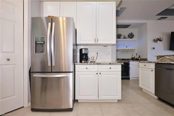 Kitchen with stainless steel appliances, light stone countertops, and white cabinetry