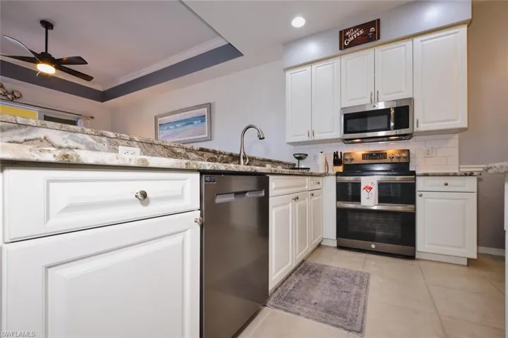 Kitchen with white cabinets, stainless steel appliances, light stone counters, ceiling fan, and crown molding