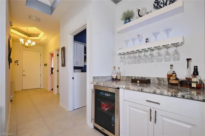 Indoor dry bar featuring open shelves, dark stone counters, beverage cooler, a raised ceiling, and white cabinets