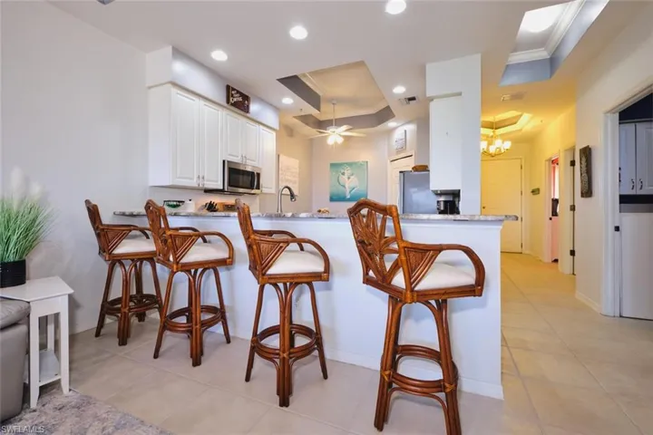 Kitchen with a tray ceiling, crown molding, a peninsula, a kitchen bar, and light countertops