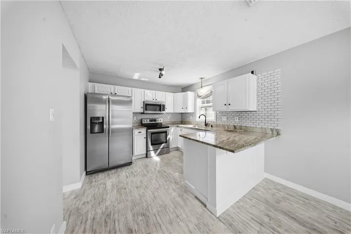 Kitchen with stainless steel appliances, white cabinetry, tasteful backsplash, a kitchen bar, and light wood finished floors