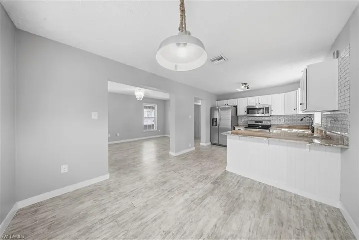 Kitchen with stainless steel appliances, white cabinets, backsplash, open floor plan, and light stone countertops