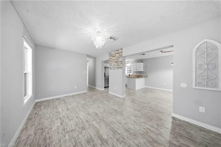 Unfurnished living room featuring light wood-type flooring, a textured ceiling, and hanging lights