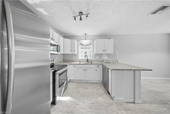 Kitchen featuring stainless steel appliances, a peninsula, tasteful backsplash, pendant lighting, and white cabinetry