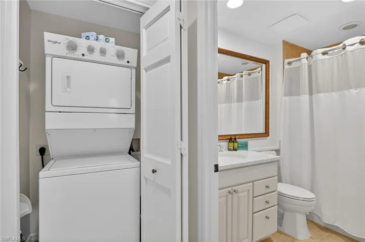 Full bathroom featuring vanity, a shower with shower curtain, stacked washer and dryer, and light tile patterned flooring
