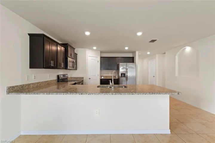 Kitchen with dark brown cabinetry, stainless steel appliances, light tile patterned floors, light stone countertops, and recessed lighting