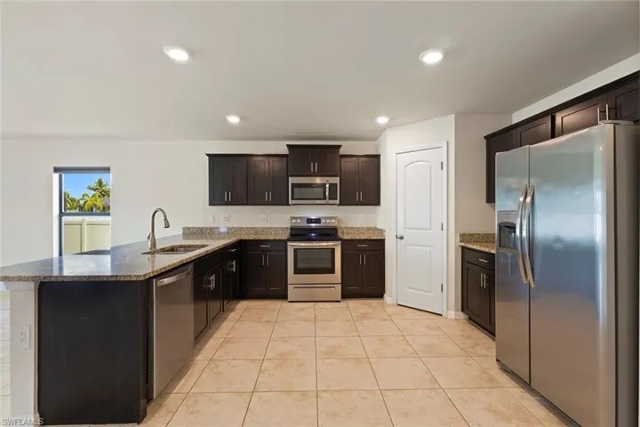 Kitchen featuring stainless steel appliances, a peninsula, dark stone counters, dark brown cabinetry, and recessed lighting