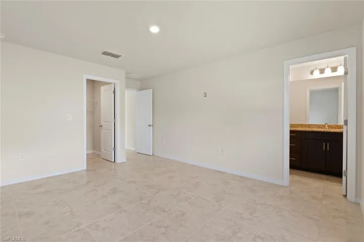 Unfurnished bedroom with a spacious closet, ensuite bathroom, light tile patterned floors, and recessed lighting