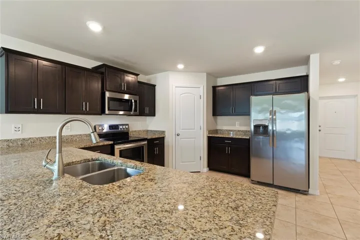Kitchen featuring stainless steel appliances, dark brown cabinets, light stone countertops, recessed lighting, and light tile patterned flooring
