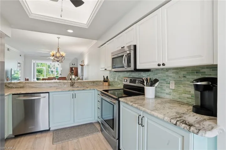 Kitchen featuring stainless steel appliances, granite counters, ceiling fan, crown molding, white cabinetry, and hanging light fixtures