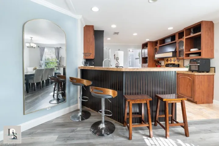 Kitchen featuring brown cabinets, a breakfast bar area, backsplash, premium range hood, and light wood-type flooring