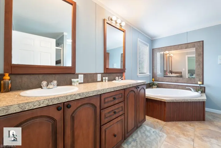 Bathroom featuring a bath, double vanity, light tile patterned flooring, tasteful backsplash, and crown molding