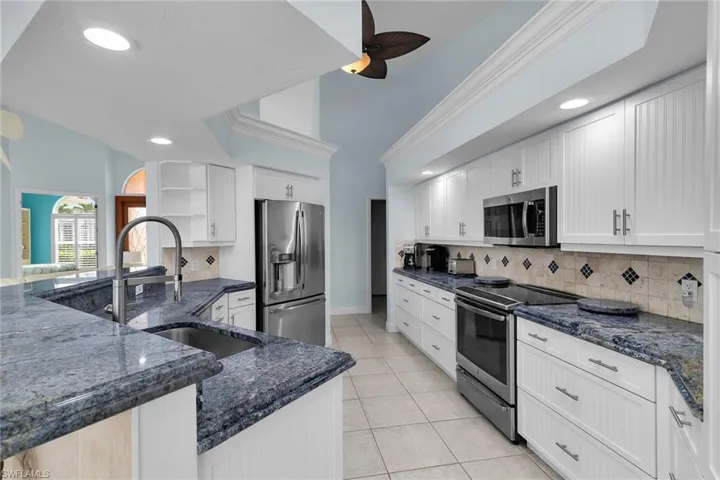 Kitchen with white cabinetry, appliances with stainless steel finishes, dark stone countertops, light tile patterned floors, and open shelves