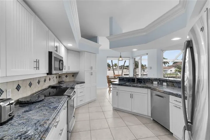 Kitchen with ornamental molding, stainless steel appliances, dark stone counters, white cabinetry, and light tile patterned floors