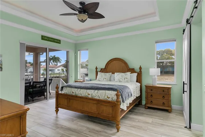 Bedroom featuring a barn door, a raised ceiling, crown molding, access to outside, and a ceiling fan