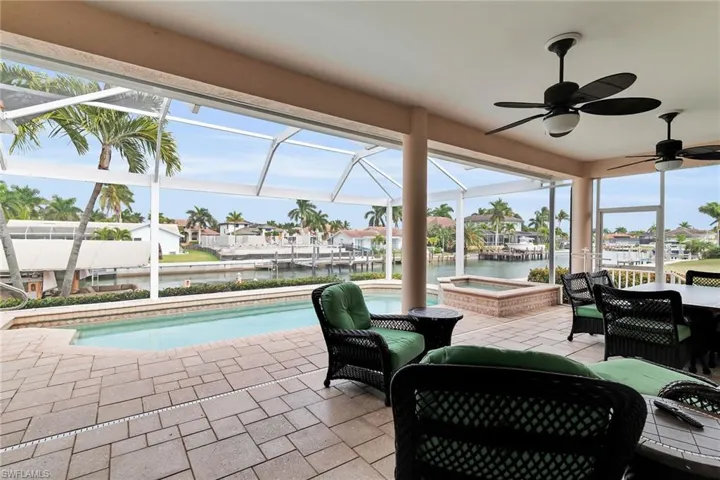 View of patio / terrace featuring a lanai, an outdoor pool, a water view, and a hot tub
