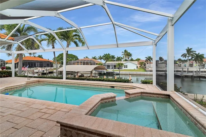 View of pool featuring a sunroom, a water view, a patio, glass enclosure, and a pool with connected hot tub