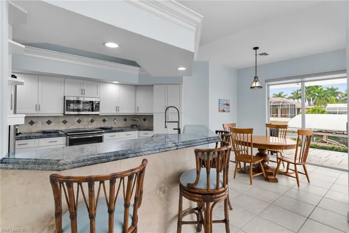 Kitchen with backsplash, a kitchen bar, stainless steel appliances, decorative light fixtures, and recessed lighting