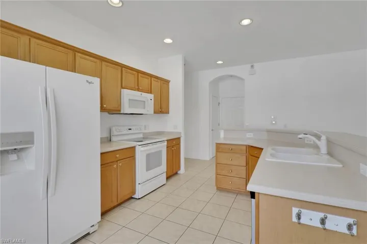 Kitchen featuring white appliances, arched walkways, light countertops, recessed lighting, and light tile patterned floors