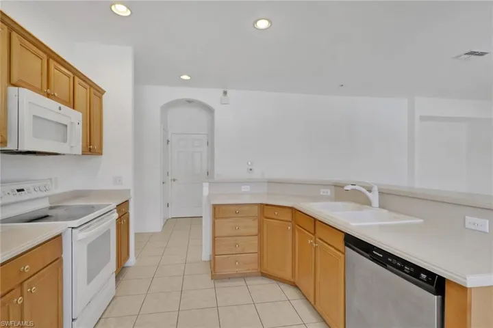 Kitchen featuring white appliances, light countertops, light tile patterned floors, recessed lighting, and arched walkways