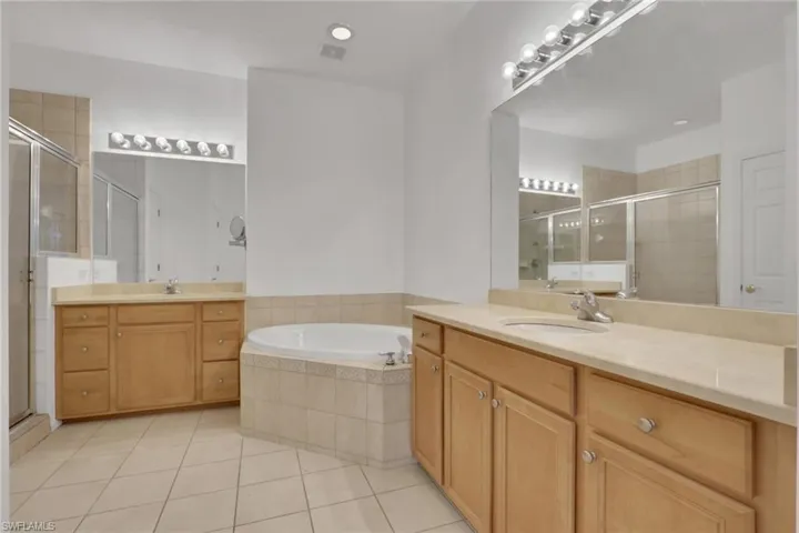 Bathroom featuring two vanities, a garden tub, a stall shower, light tile patterned floors, and recessed lighting
