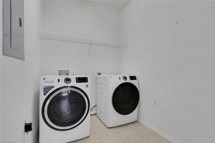 Washroom featuring electric panel, light tile patterned floors, and separate washer and dryer
