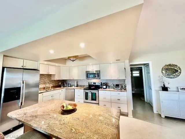 Kitchen with sink, white cabinetry, light stone counters, appliances with stainless steel finishes, and a kitchen breakfast bar