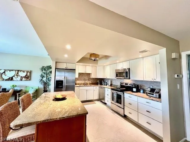 Kitchen featuring appliances with stainless steel finishes, a breakfast bar, white cabinetry, sink, and light stone counters