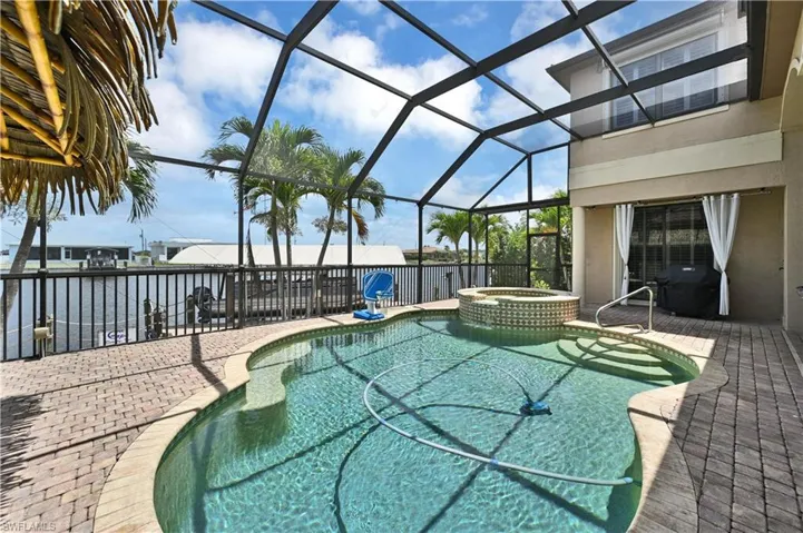 Screened outdoor living area featuring a free-form swimming pool with integrated spa, paver patio, and canal frontage