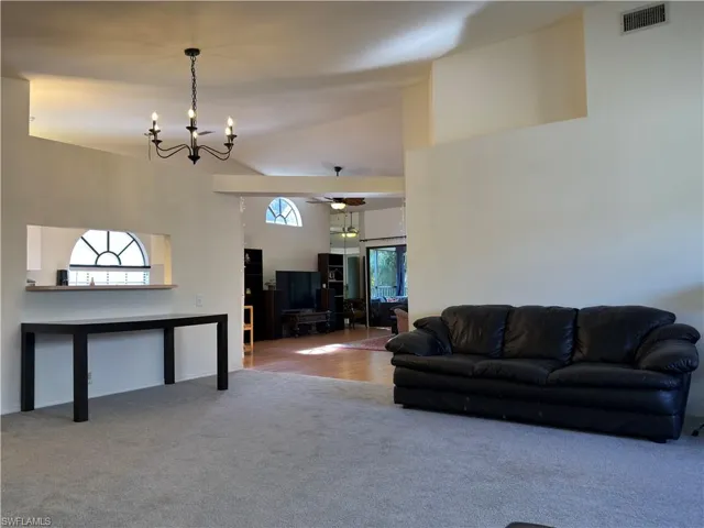 Carpeted living area with a chandelier, a ceiling fan, and vaulted ceiling