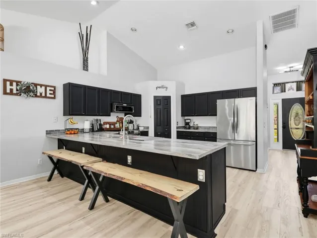 Kitchen featuring dark cabinetry, a breakfast bar, a peninsula, stainless steel appliances, and light stone counters