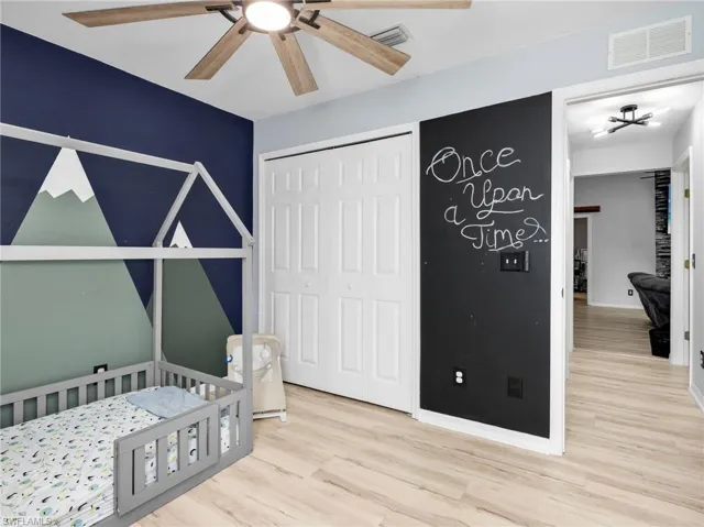 Bedroom featuring light wood finished floors, a closet, a nursery area, and ceiling fan