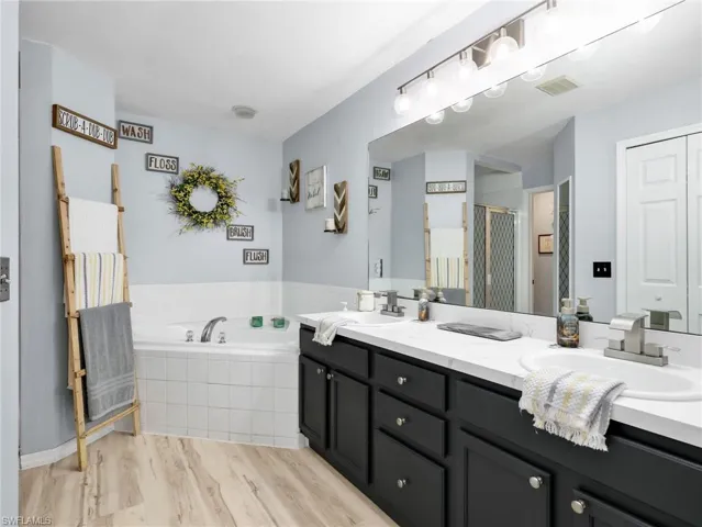 Bathroom featuring double vanity, a bath, light wood-style flooring, and a shower stall