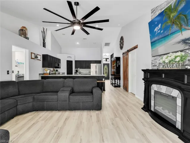 Living room with a barn door, ceiling fan, vaulted ceiling, light wood-type flooring, and recessed lighting