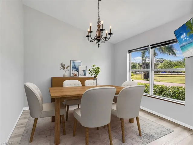 Virtually staged dining room with a chandelier, light wood-style floors, and vaulted ceiling
