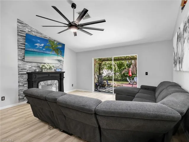 Living room featuring vaulted ceiling, light wood-type flooring, a fireplace, and ceiling fan