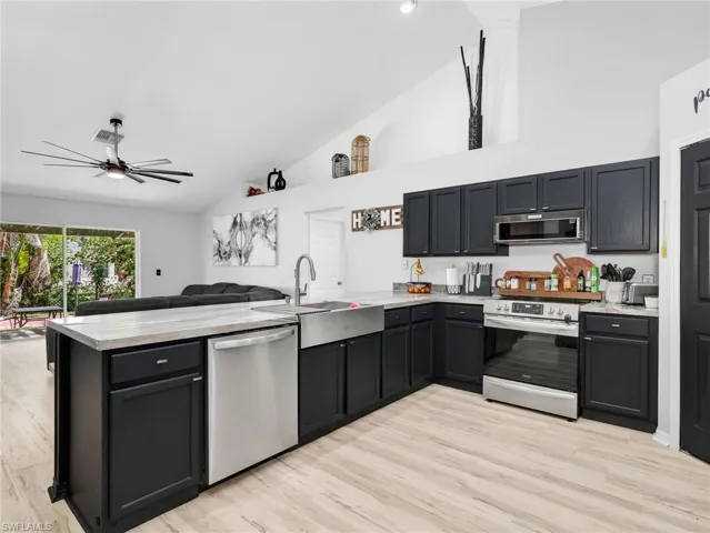 Kitchen featuring dark cabinetry, a peninsula, stainless steel appliances, ceiling fan, and lofted ceiling