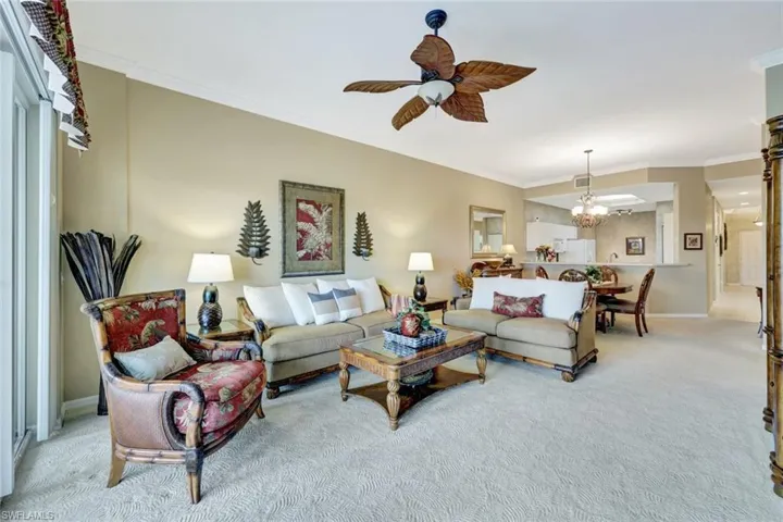 Carpeted living room featuring crown molding and ceiling fan with notable chandelier