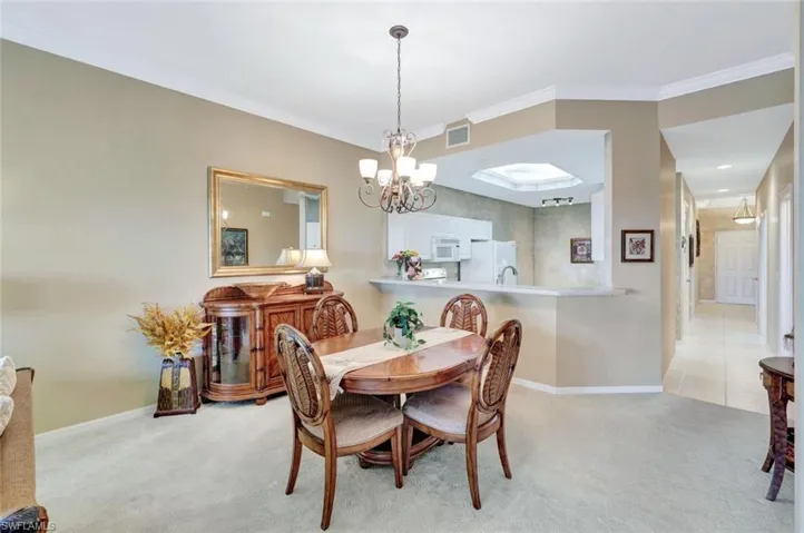 Dining room featuring a notable chandelier, ornamental molding, and light colored carpet